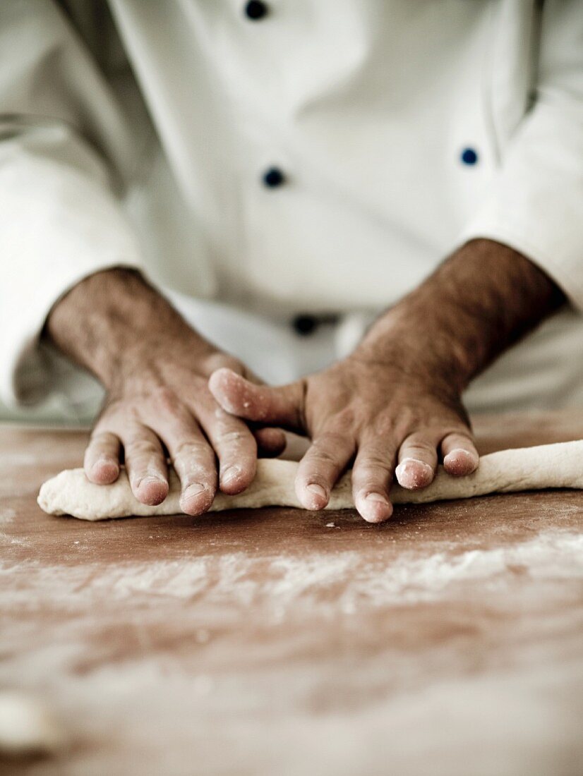 A chef rolling out gnocchi dough on a floured work surface