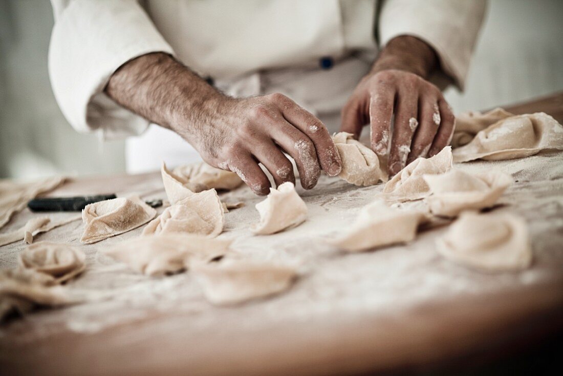 A chef rolling fresh tortellini in flour