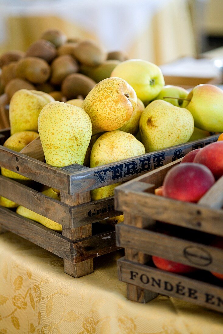 A wooden box of pears, between a box of nectarines and one of kiwis