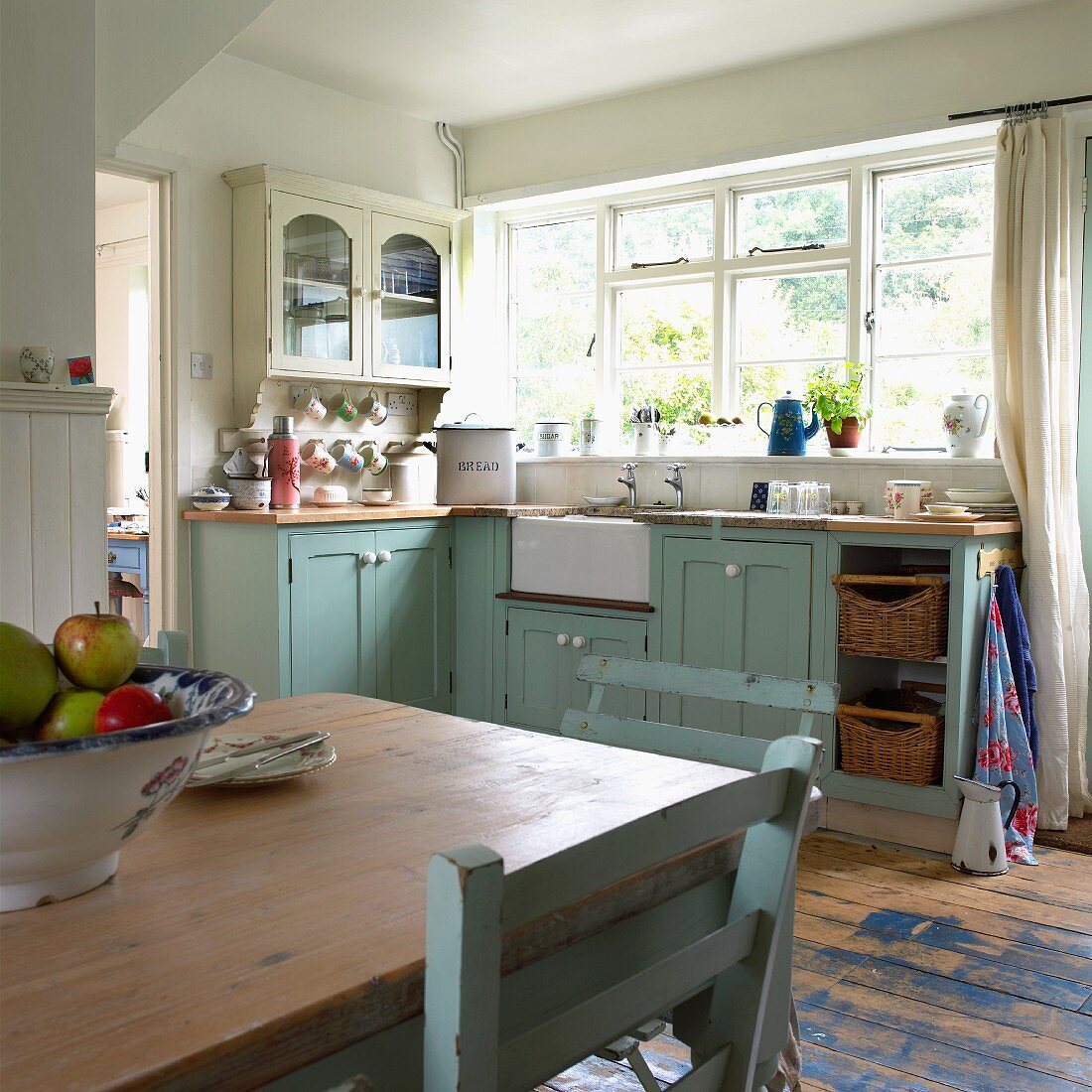 Old, pastel blue kitchen-dining room in English country-house style; bowl of apples on dining table in foreground