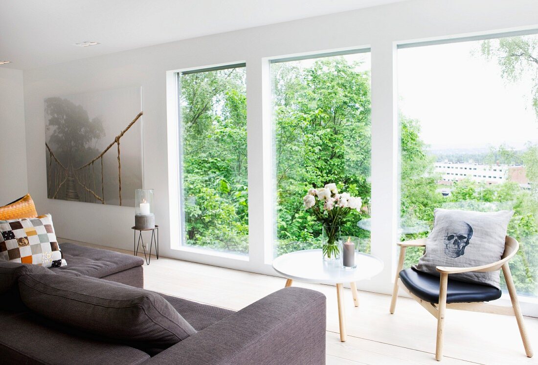 Polstersofa und Tisch mit Blumenstrauss neben Retro Stuhl vor raumhohe Fenster mit Stadtblick