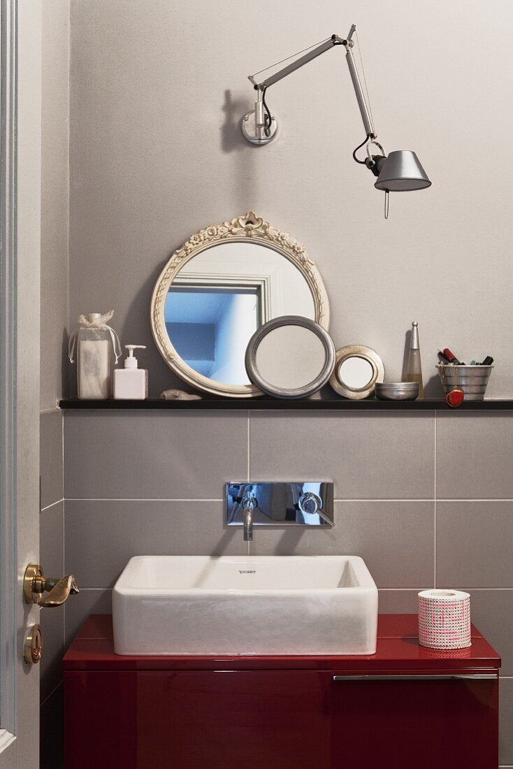 Washstand with countertop trough on red base unit below designer wall lamp and collection of round mirrors