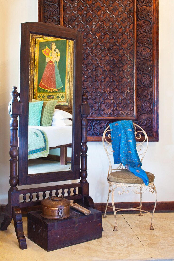 Wood-framed cheval glass and vintage metal chair in front of carved panel in corner of room