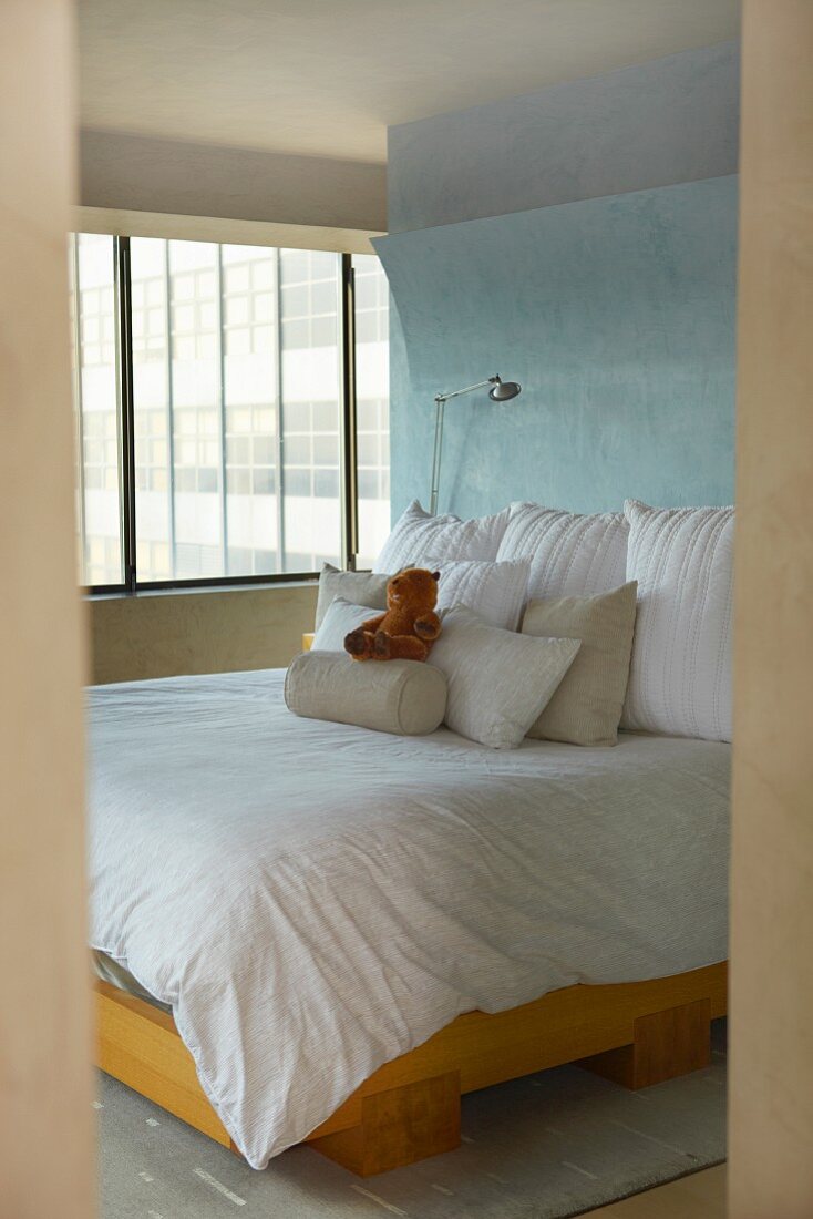 View through doorway to double bed with pillows stack of bright blue wall