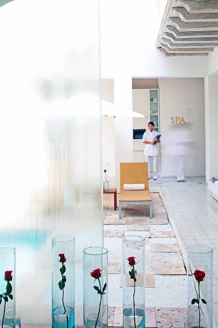 Red roses in glass vases on floor of courtyard and member of staff in entrance to spa