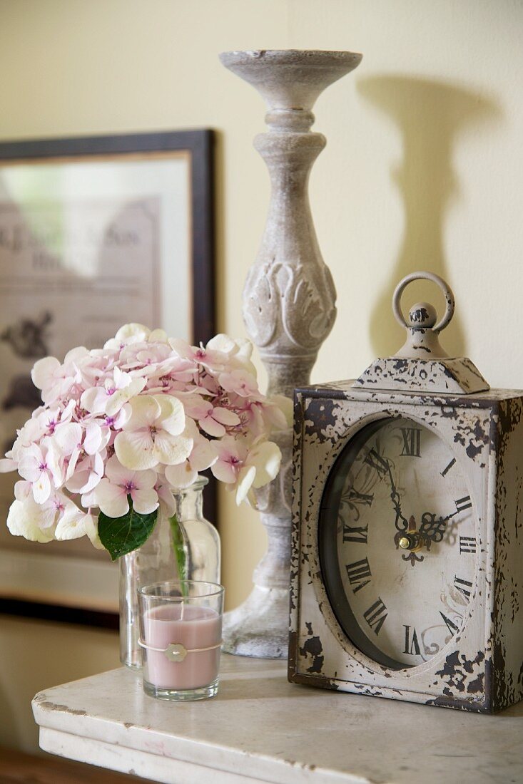 Antique table clock, candlestick, hydrangea flower and scented candle on shelf