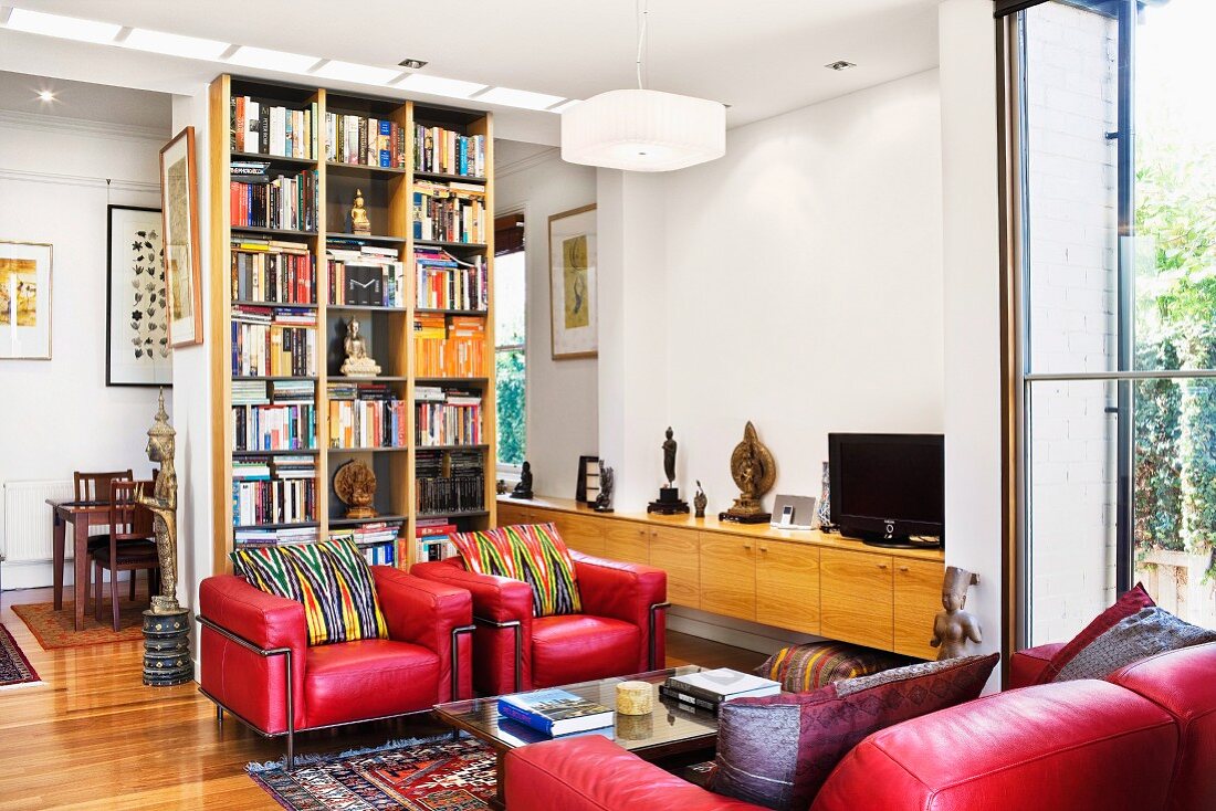 Red leather furniture in front of a book case doubling as a room divider