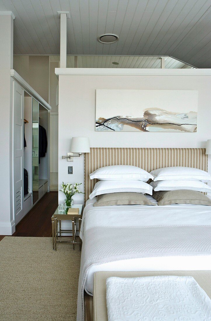 Modernes Gemälde über gestreiftem Bettkopfende in elegantem Schlafzimmer; im Hintergrund der begehbare Kleiderschrank