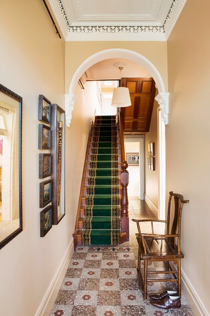 Nostalgischer Fliesenboden im Flur mit Rundbogen vor Treppe mit Teppichläufer in einem herrschaftlichem Haus mit Stuckdecke