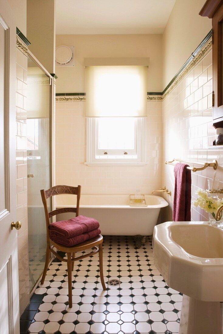 Blick durch offene Tür auf antiken Holzstuhl und gemusterten Fliesenboden im Vintage Bad