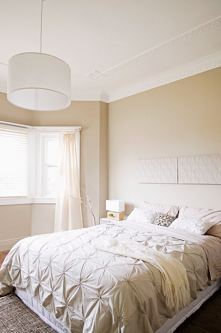 Doppelbett mit eleganter Tagesdecke und schlichte Hängeleuchte mit weißem Lampenschirm in beige getöntem Schlafzimmer mit traditionellem Flair