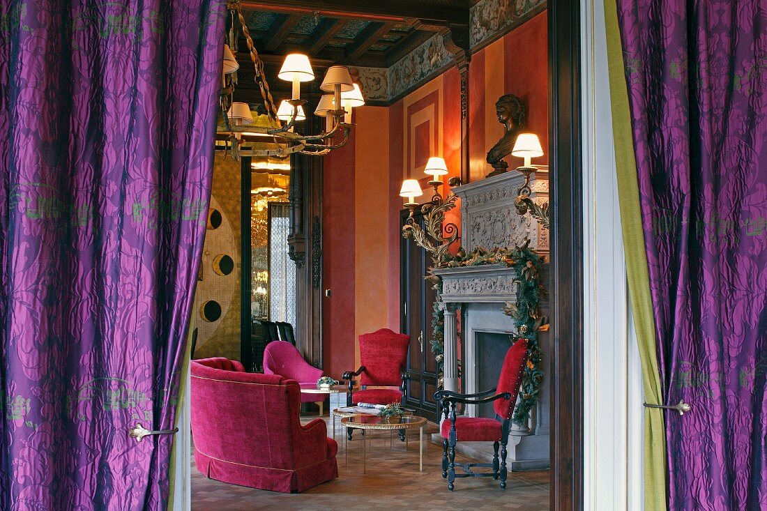 View through purple curtains into flamboyant Renaissance salon with red upholstered seating in front of fireplace