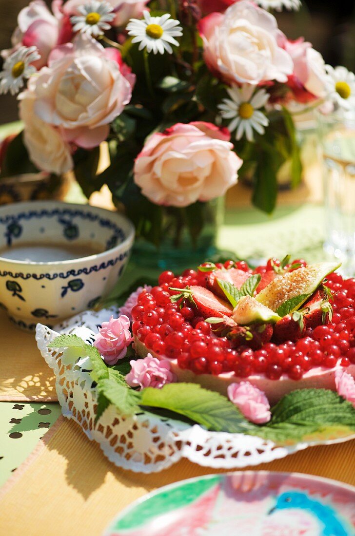 Johannisbeerkuchen auf und Blumenstrauss auf gedecktem Tisch im Freien