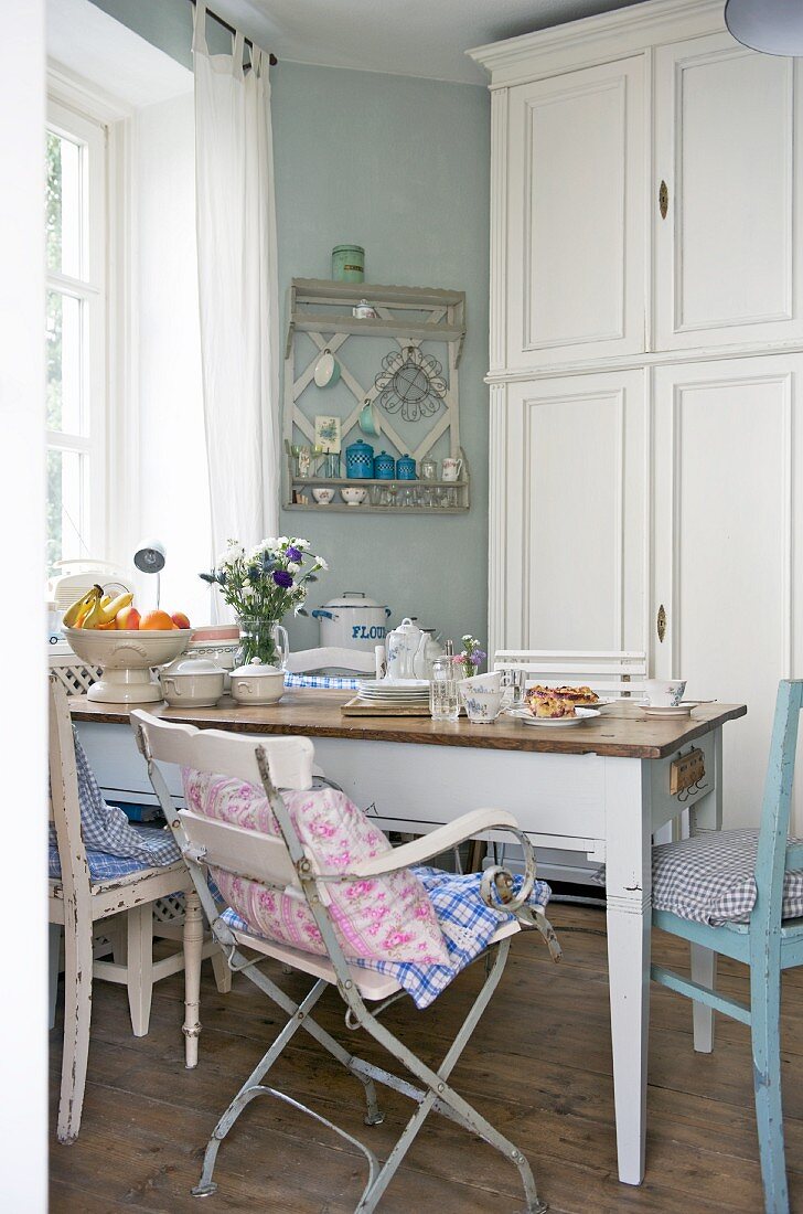 Various chairs around old table in front of cupboard