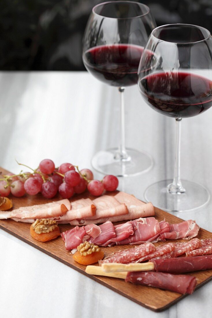 A selection of cold meats with grapes and two glasses of red wine