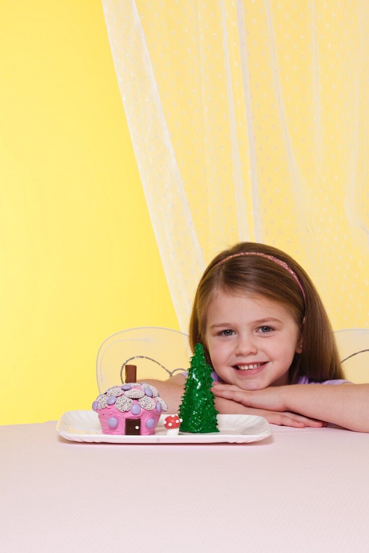 A Little Girl Wearing Fairy Wings Next to a Fairy House Cake