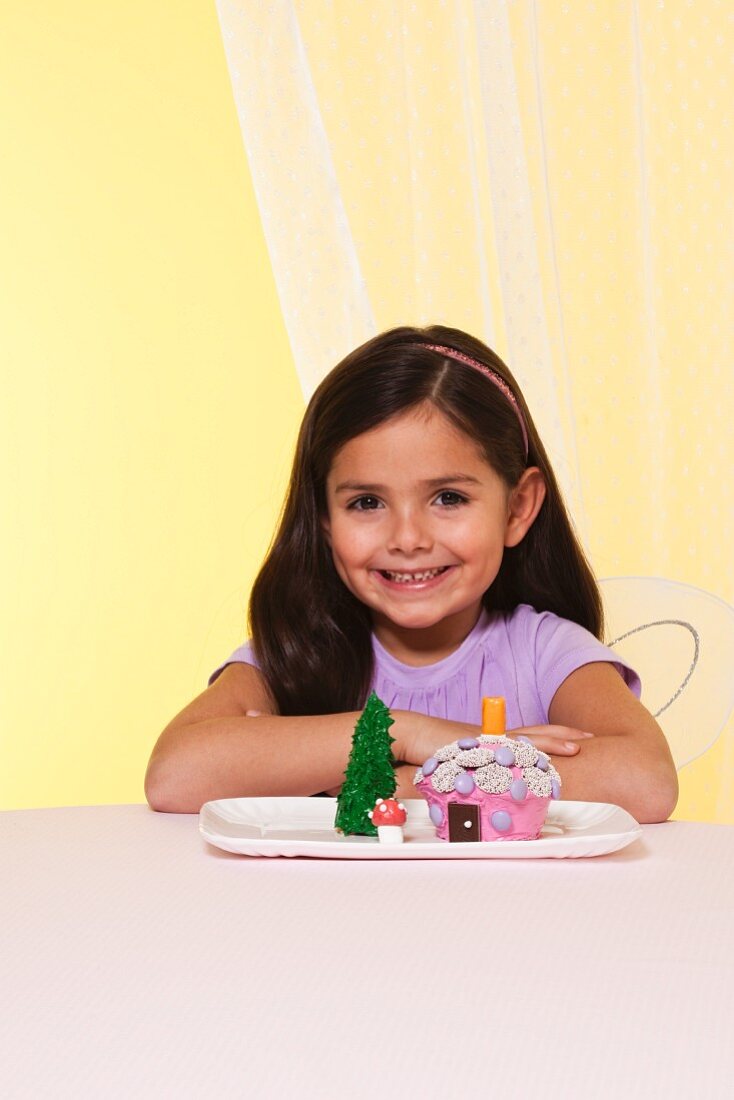 A Little Girl with Dark Hair Wearing Fairy Wings Next to a Fairy House Cake