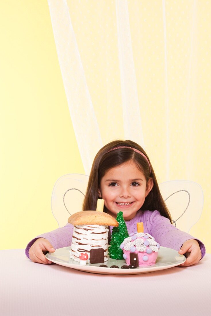 A Little Girl Wearing Fairy Wings Smiling by a Plate of Fairy House Cakes