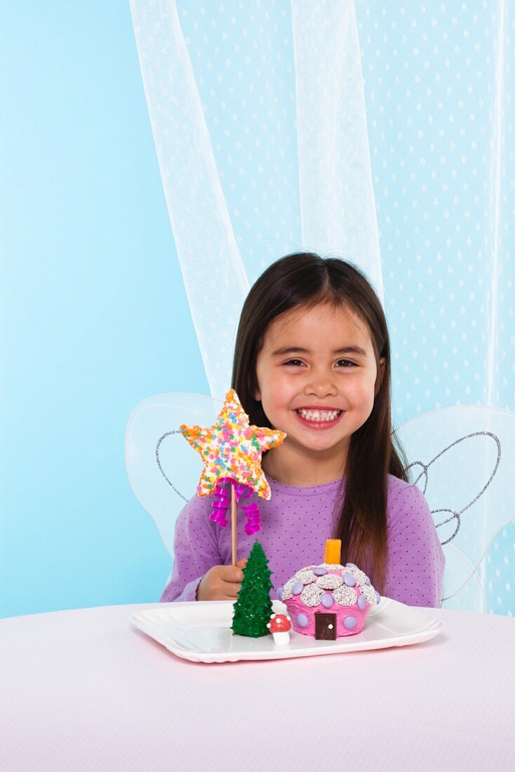 Mädchen mit Engelsflügeln, sternförmigem Cake Pop und Fairy House Cakes auf einem Teller
