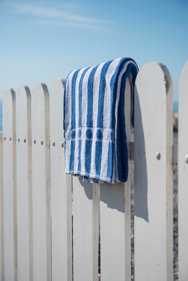 Blau-weiss gestreiftes Handtuch auf einem weissen Holzzaun am Strand