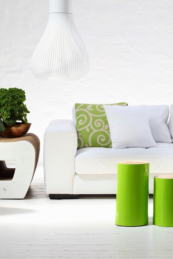 Green-varnished, cylindrical side tables in front of white sofa and designer pendant lamp with white slatted lampshade