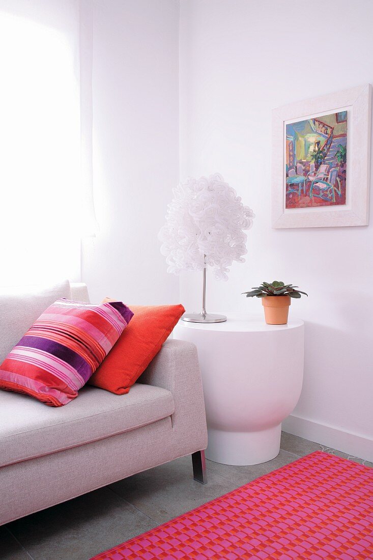 Pale sofa and white side table with designer table lamp combined with colourful scatter cushions and pink rug