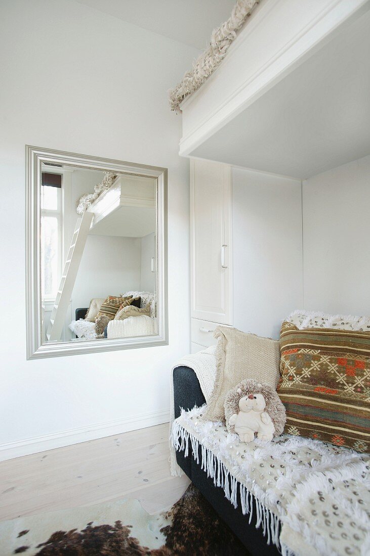 Loft bed and sofa in corner of room next to wall-mounted mirror