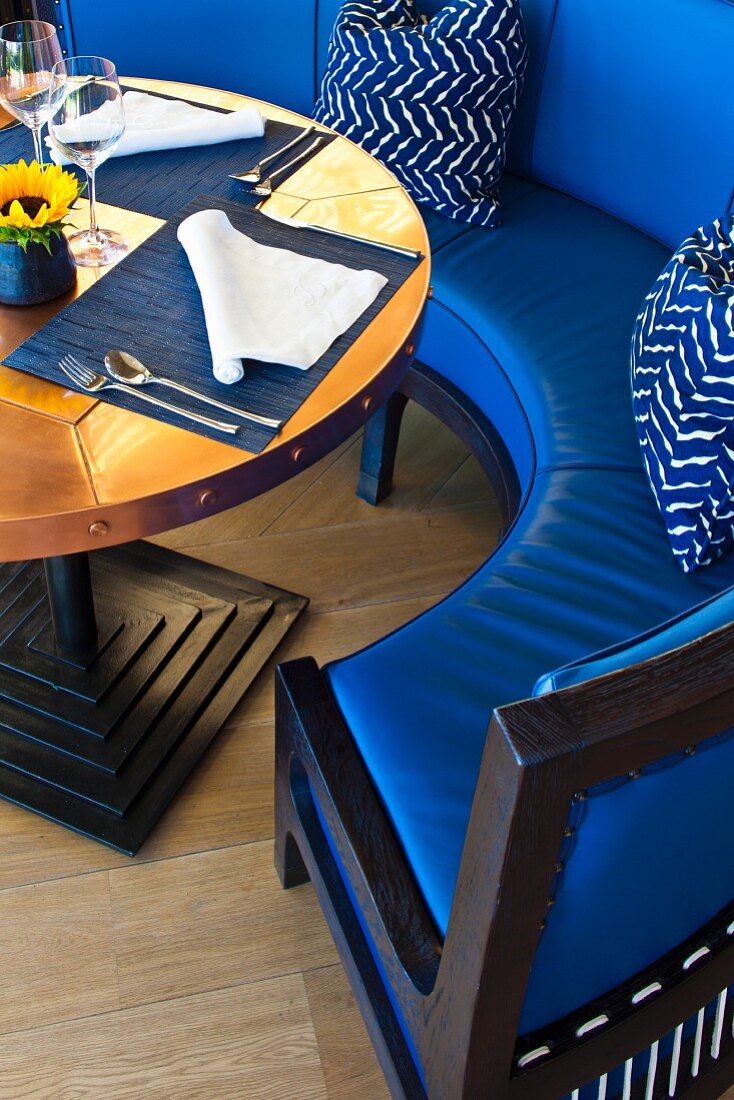 Geschwungene Sitzbank mit blauem Lederbezug vor Tisch mit Gedecken
