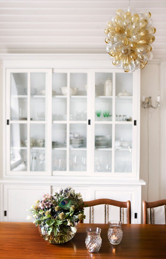 Chandelier of glass pods in various colours above traditional dining table; glass-fronted dresser in background