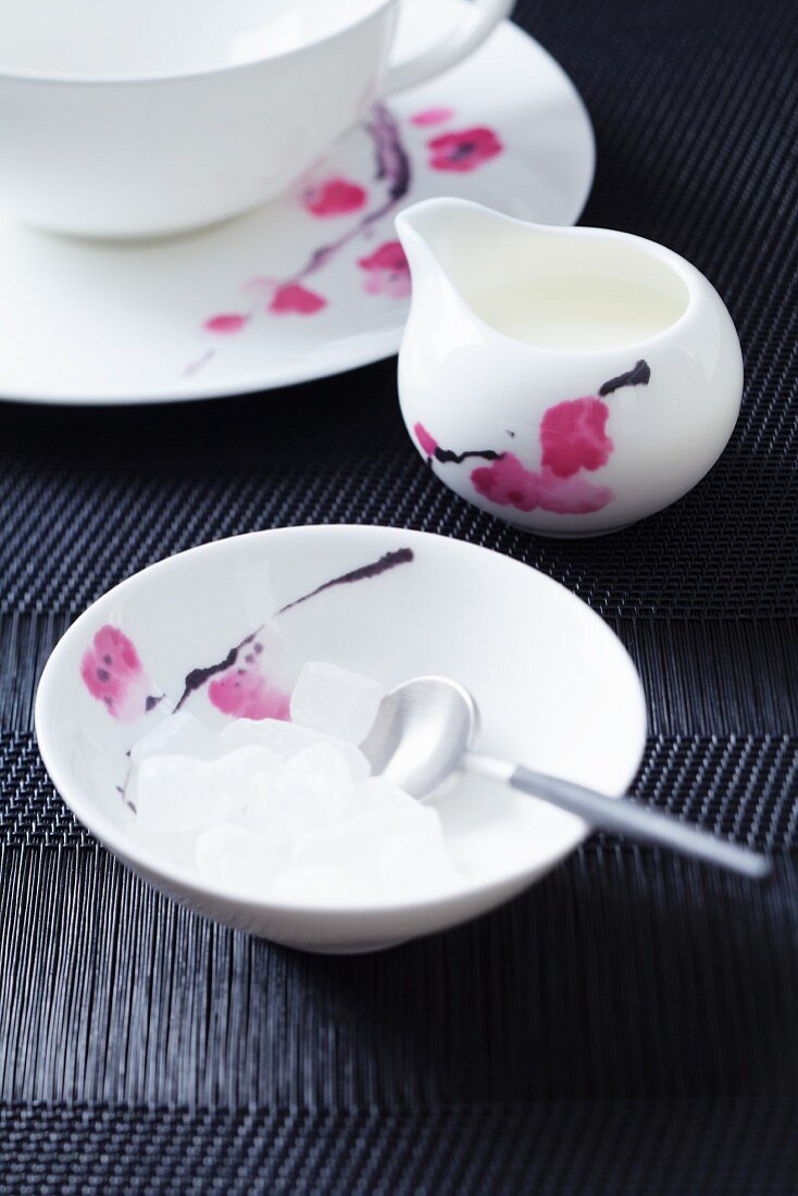 A teacup, a small milk jug and a sugar bowl of white rock sugar, all with a flower design