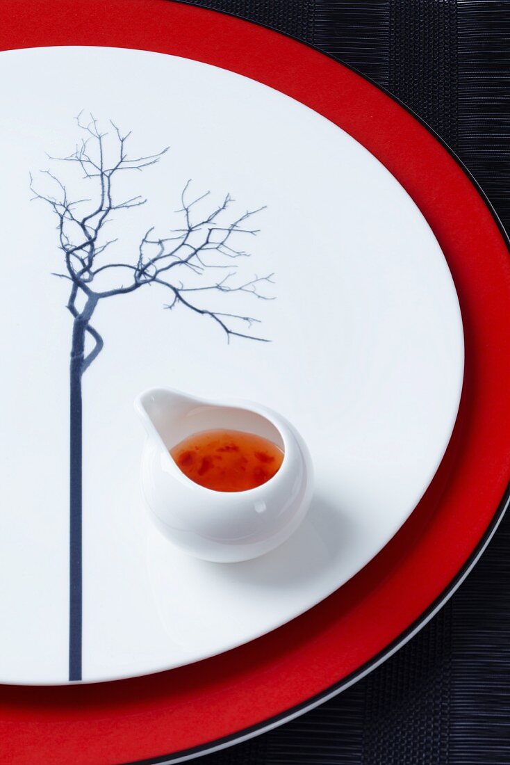 A plate decorated with a tree and with a pot of Asian sauce