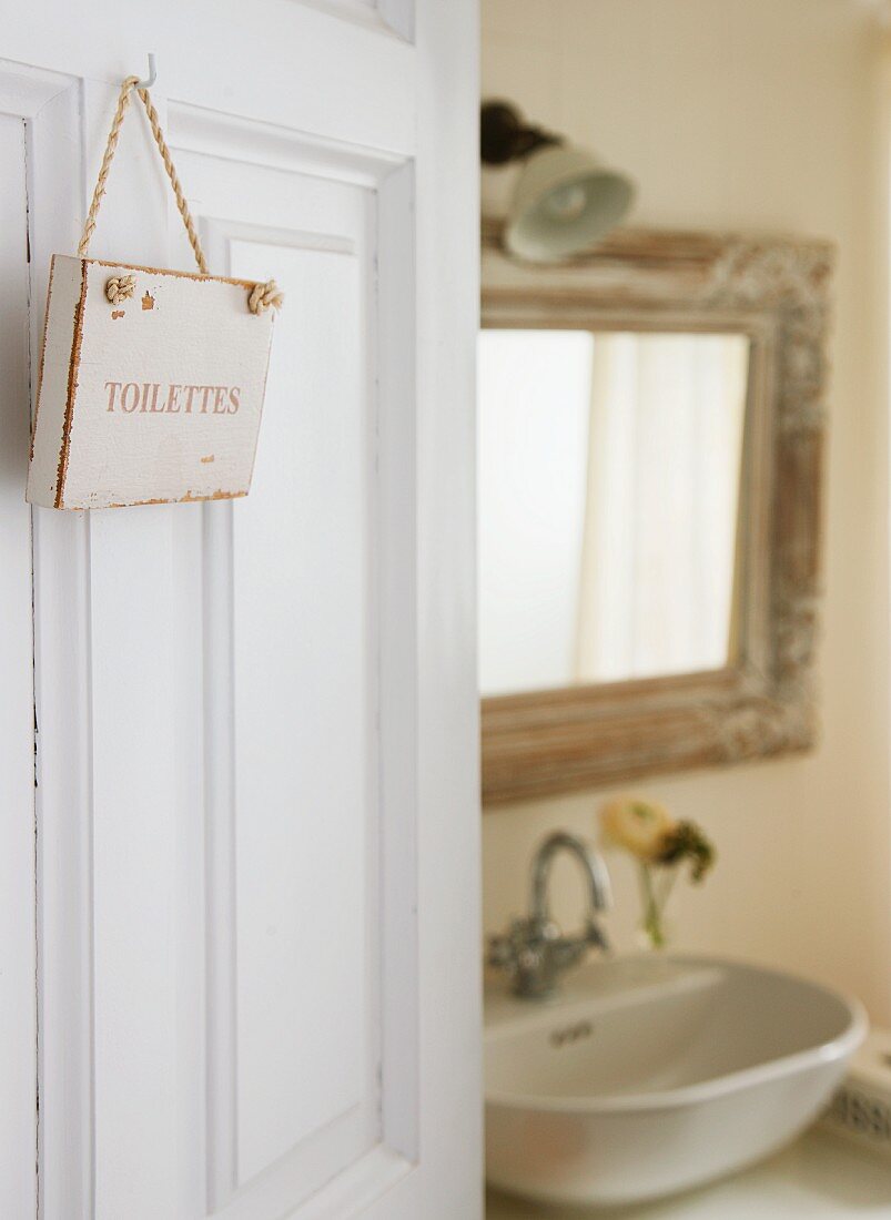 Blick durch offene Tür mit aufgehängtem Toilettenschild auf Waschtisch und Spiegel
