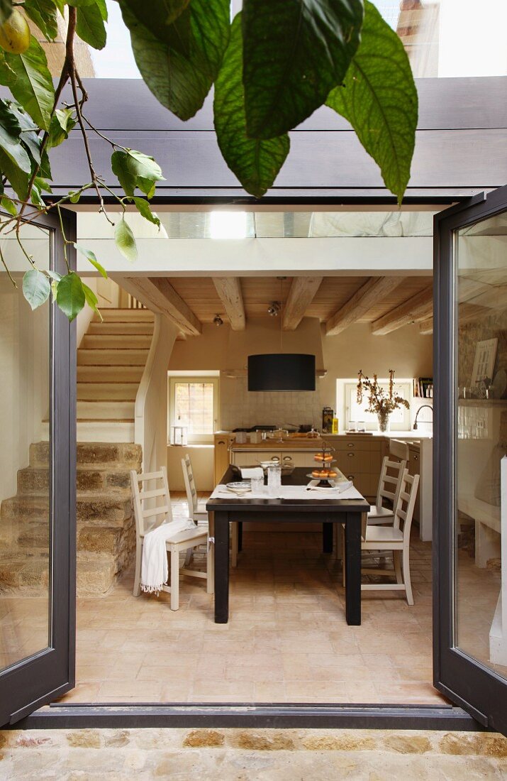View through open terrace door into modern house with dining area and kitchen next to masonry staircase