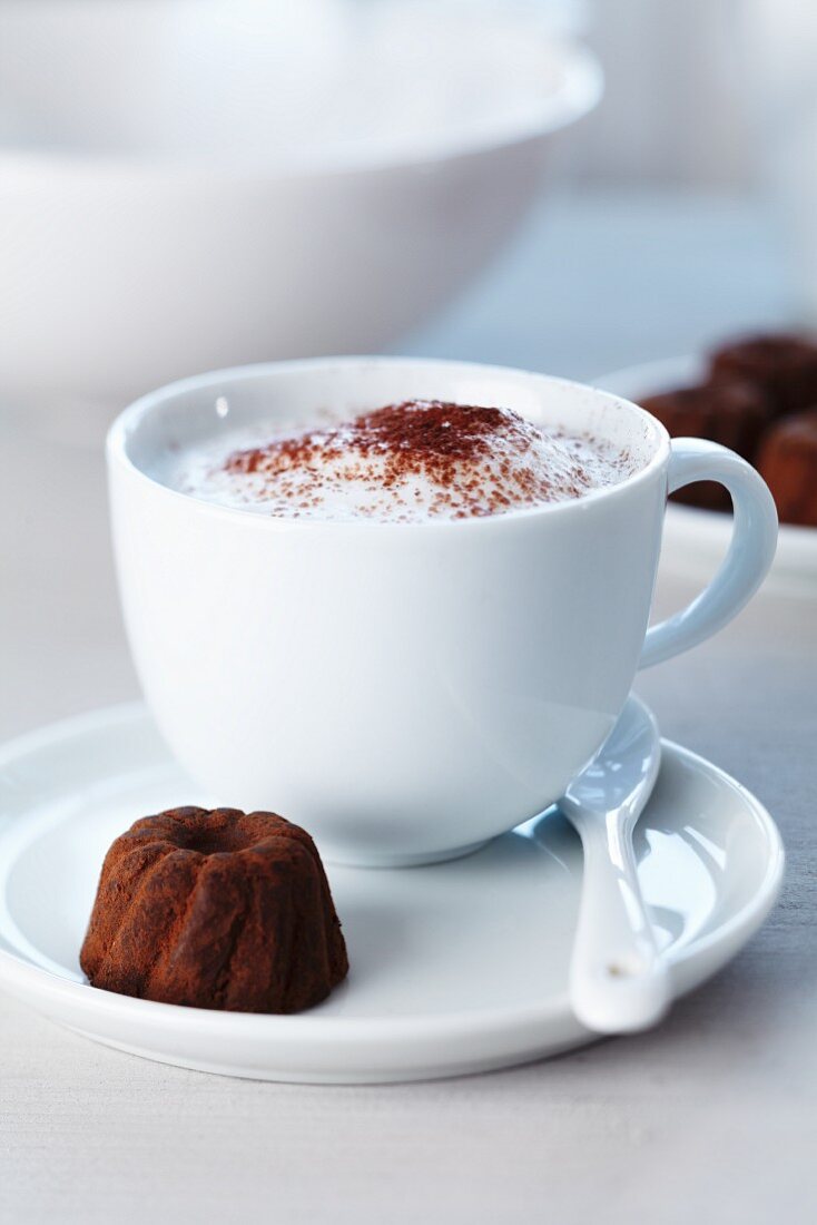 A cup of cappuccino and a praline in the shape of a ring cake