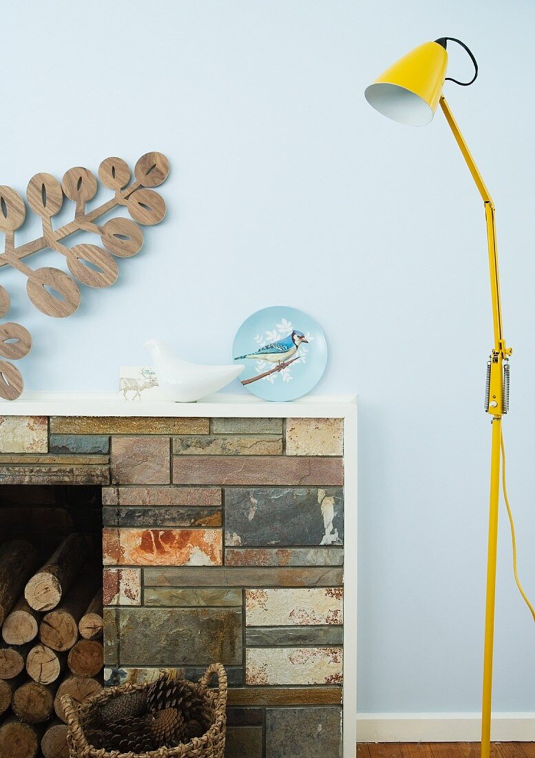 Yellow, retro floor lamp next to an open fireplace with natural stone apron in front of a bright blue wall