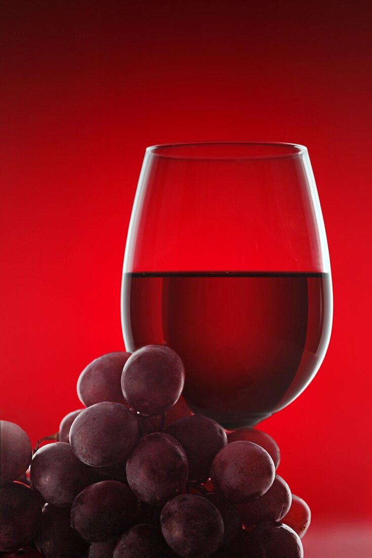 Rotweinglas und rote Trauben vor rotem Hintergrund