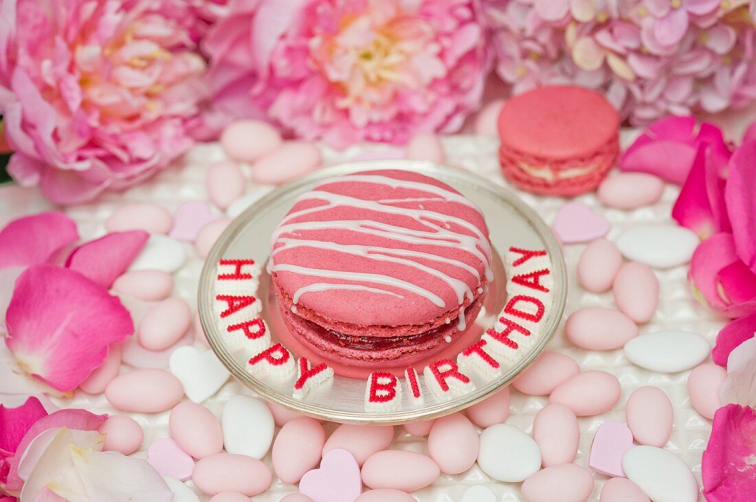 Pink Macaron mit Zuckerstreifen auf Silberteller, umgeben von Zuckermandeln, Pfingstrosen und Rosenblättern