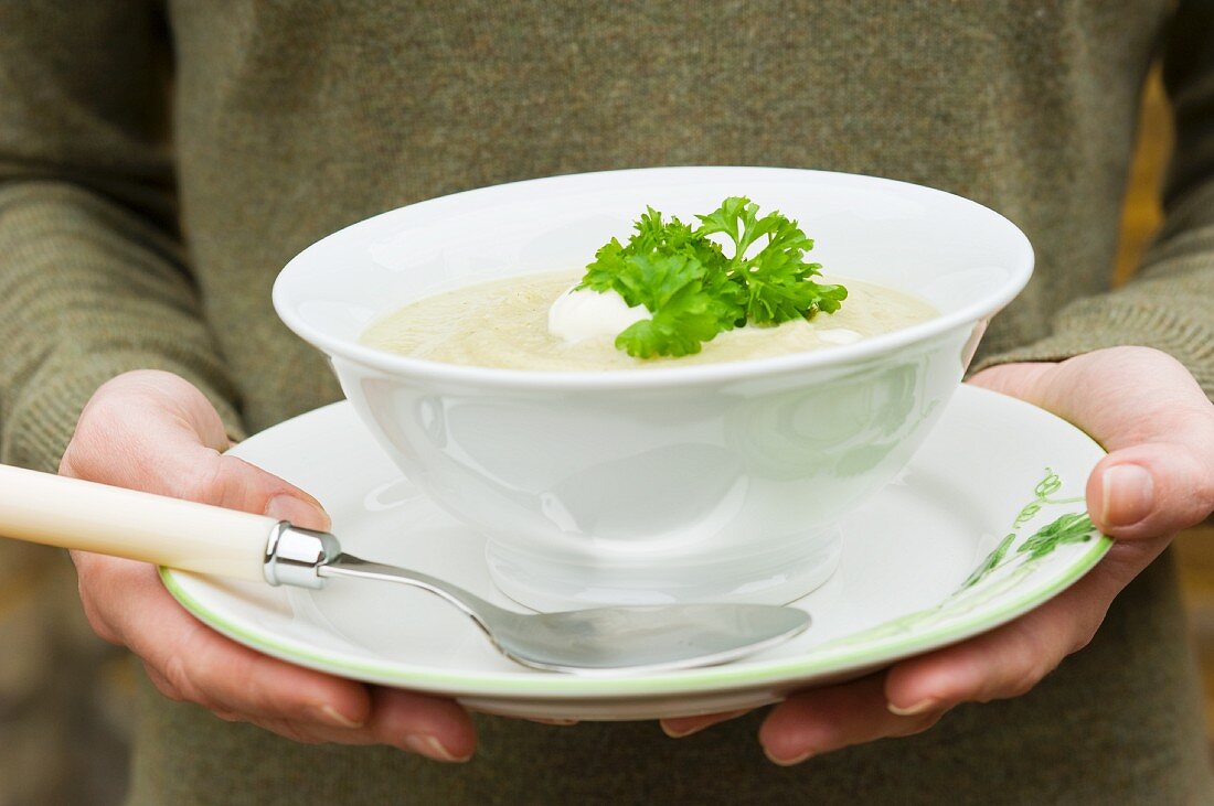 A woman holding a bowl of celery soup with crème fraîche and parsley