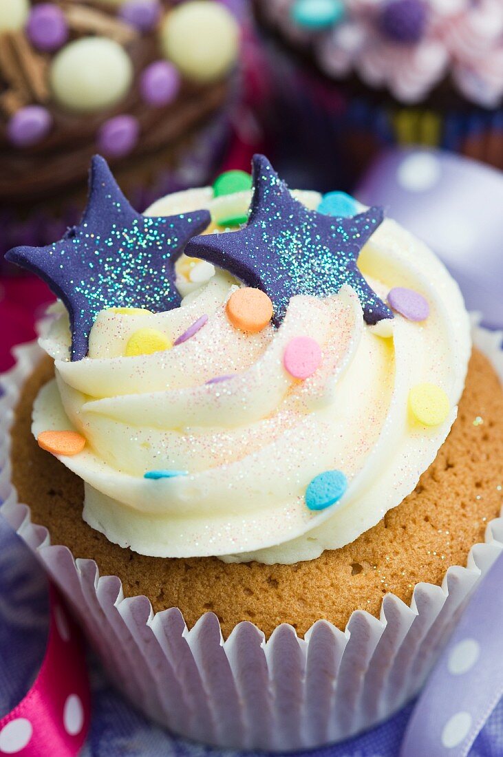 A vanilla cupcake with blue stars, glitter and sugar confetti