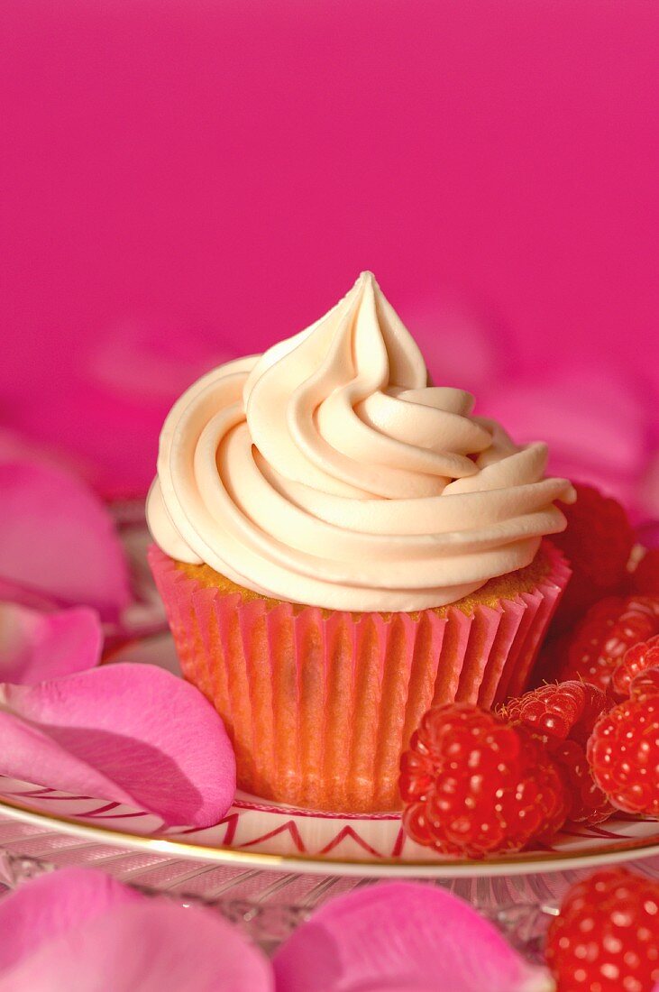 A cupcake with vanilla icing, raspberries and rose petals