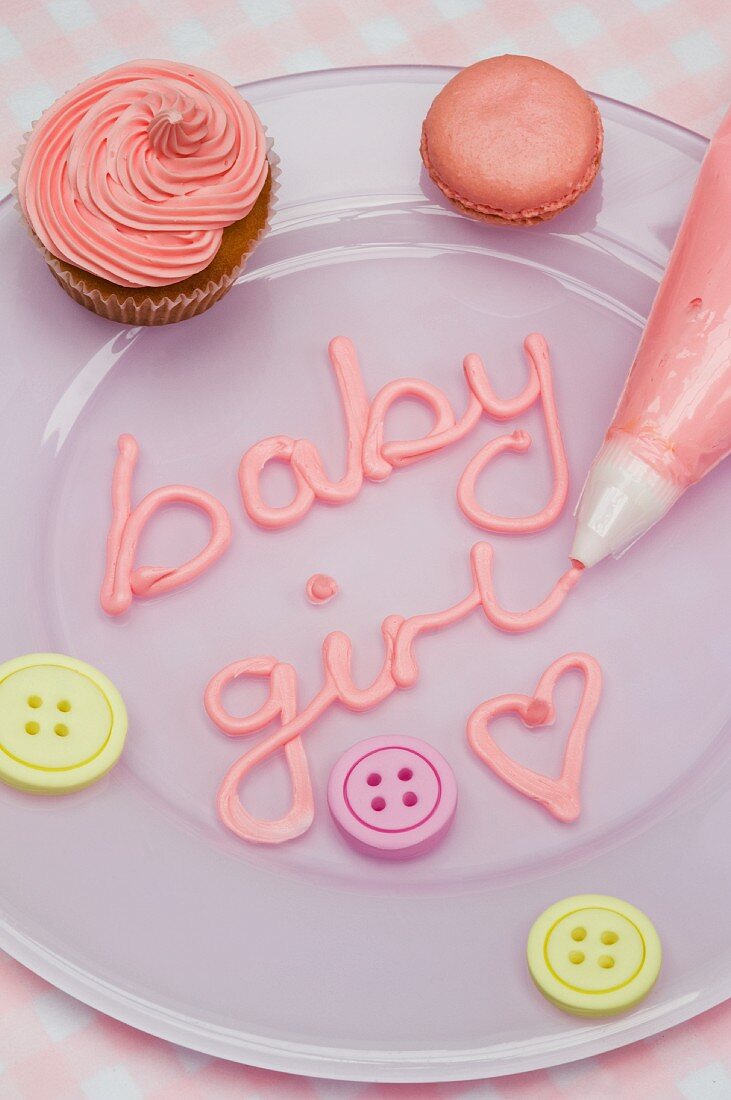 Rosa Cupcake, Macaron und Zuckerschrift mit Spritztüte für eine Babyparty