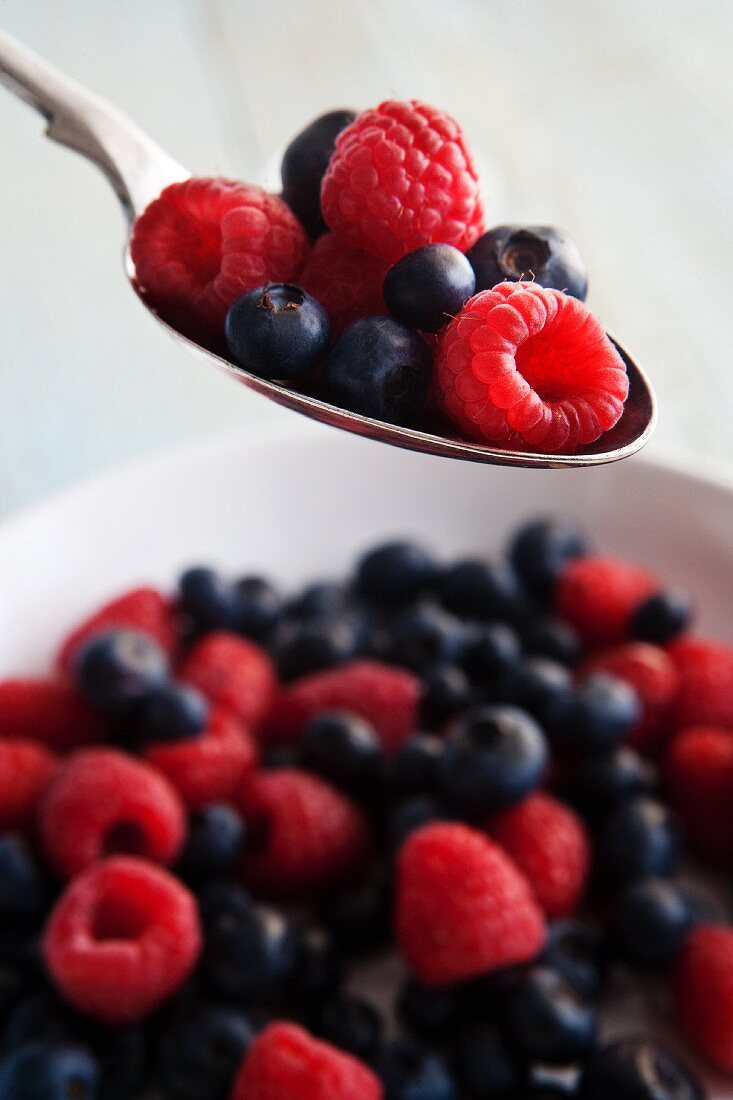 Raspberries and blueberries on a spoon and in a bowl