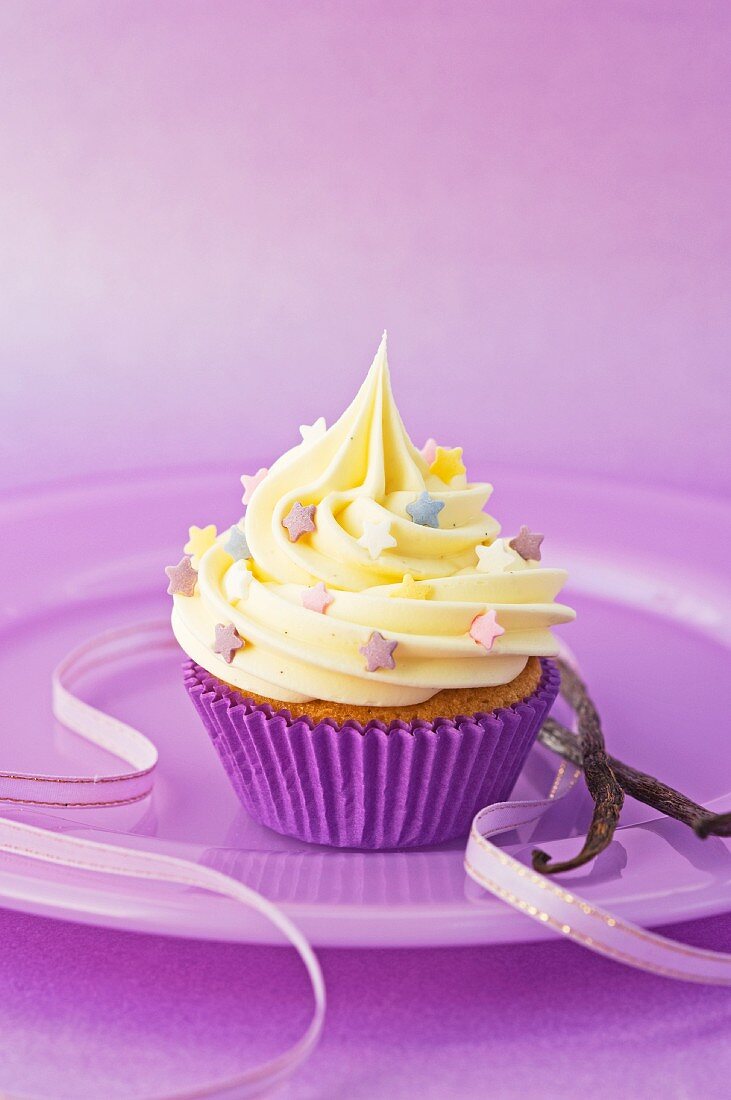 Vanille-Cupcake mit bunten Zuckersternchen auf lila Teller mit Schleife