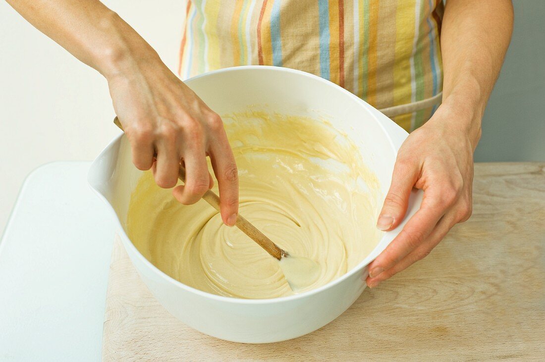 A woman mixes batter with a wooden spoon in a bowl