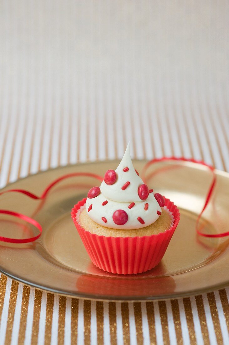 A vanilla cupcake with red chocolate beans in a red plastic case for a party