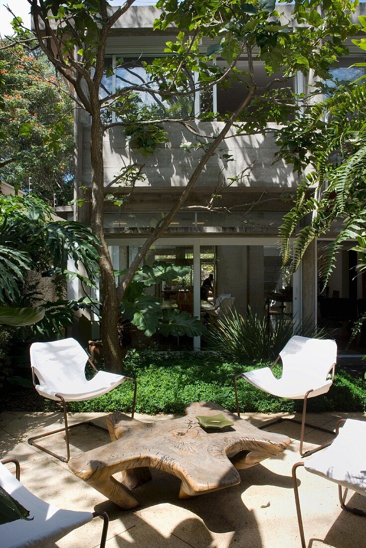 Chairs with canvas seats and star-shaped tree trunk table on Mediterranean terrace of house with large windows