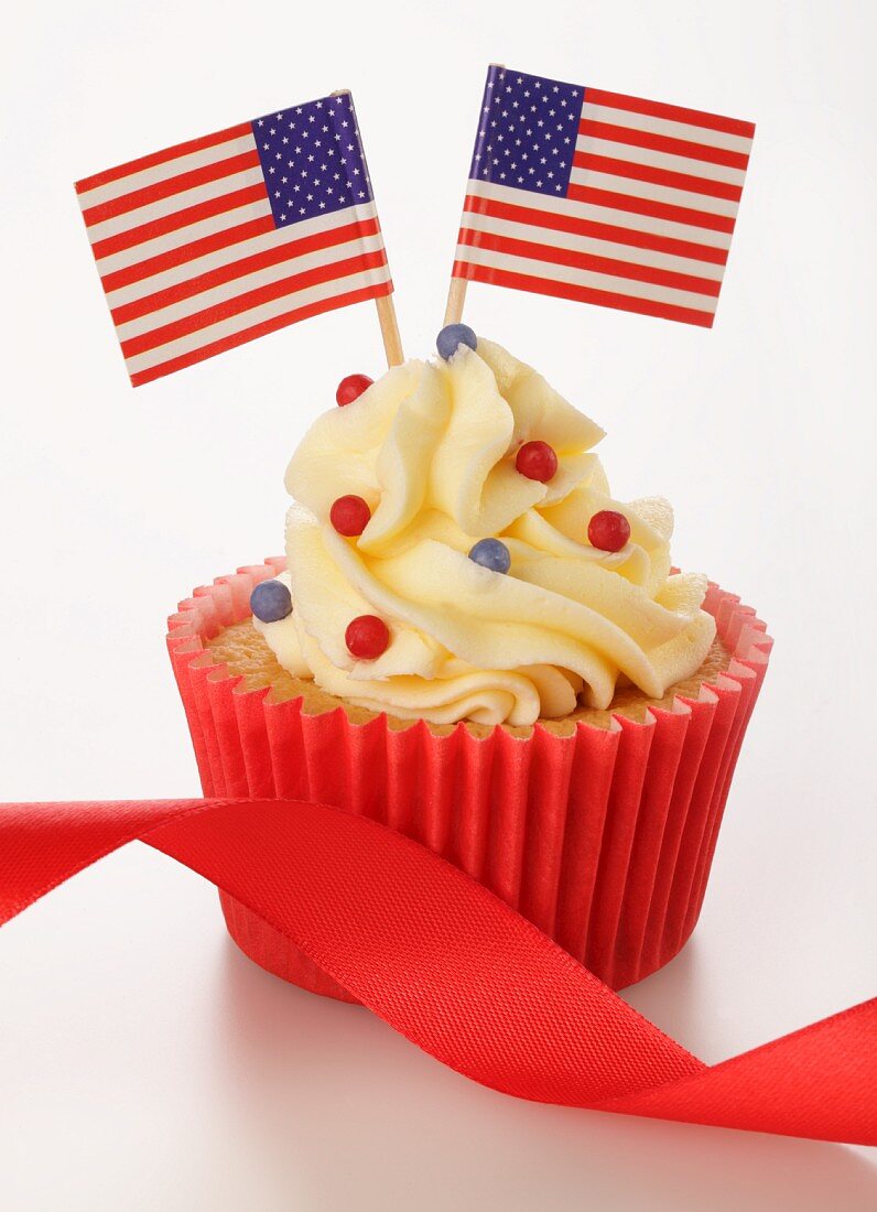 A cupcake decorated with US flags and a red ribbon