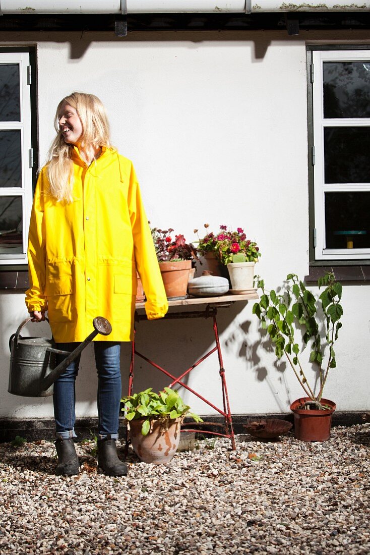 Blonde woman watering potted plants in front of house