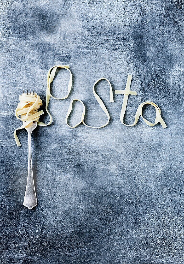 Ribbon pasta wrapped around a fork and spelling out the word pasta