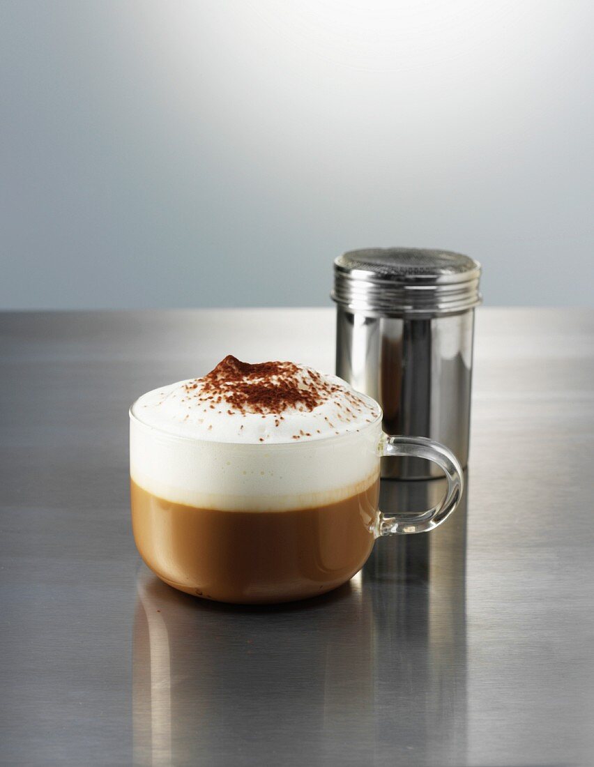 Cappuccino mit Kakaostreuer auf polierter Metallplatte